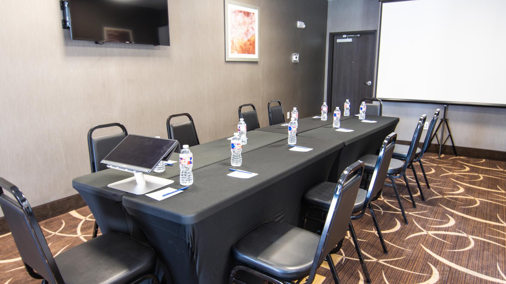 A meeting room with a long table, black chairs, bottled water, notepads, TV screen, and projection screen at Meeting Space in Houston.