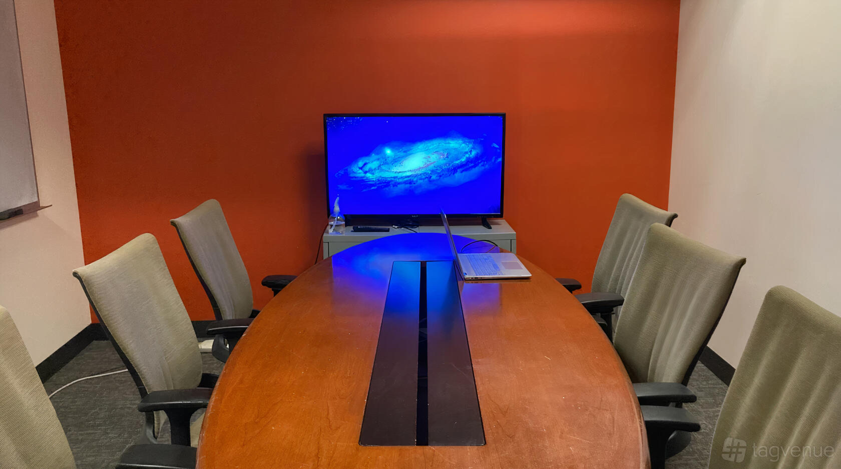 A meeting room with a wooden oval table, six office chairs, and a wall-mounted screen at SURF Incubator.