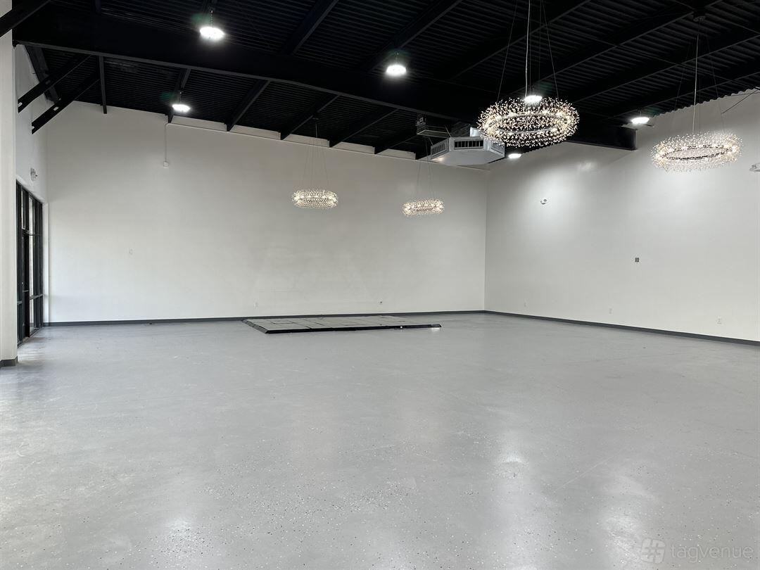 An event venue with polished concrete floors, white walls, and modern chandeliers at BLuxxx Events & Rentals.