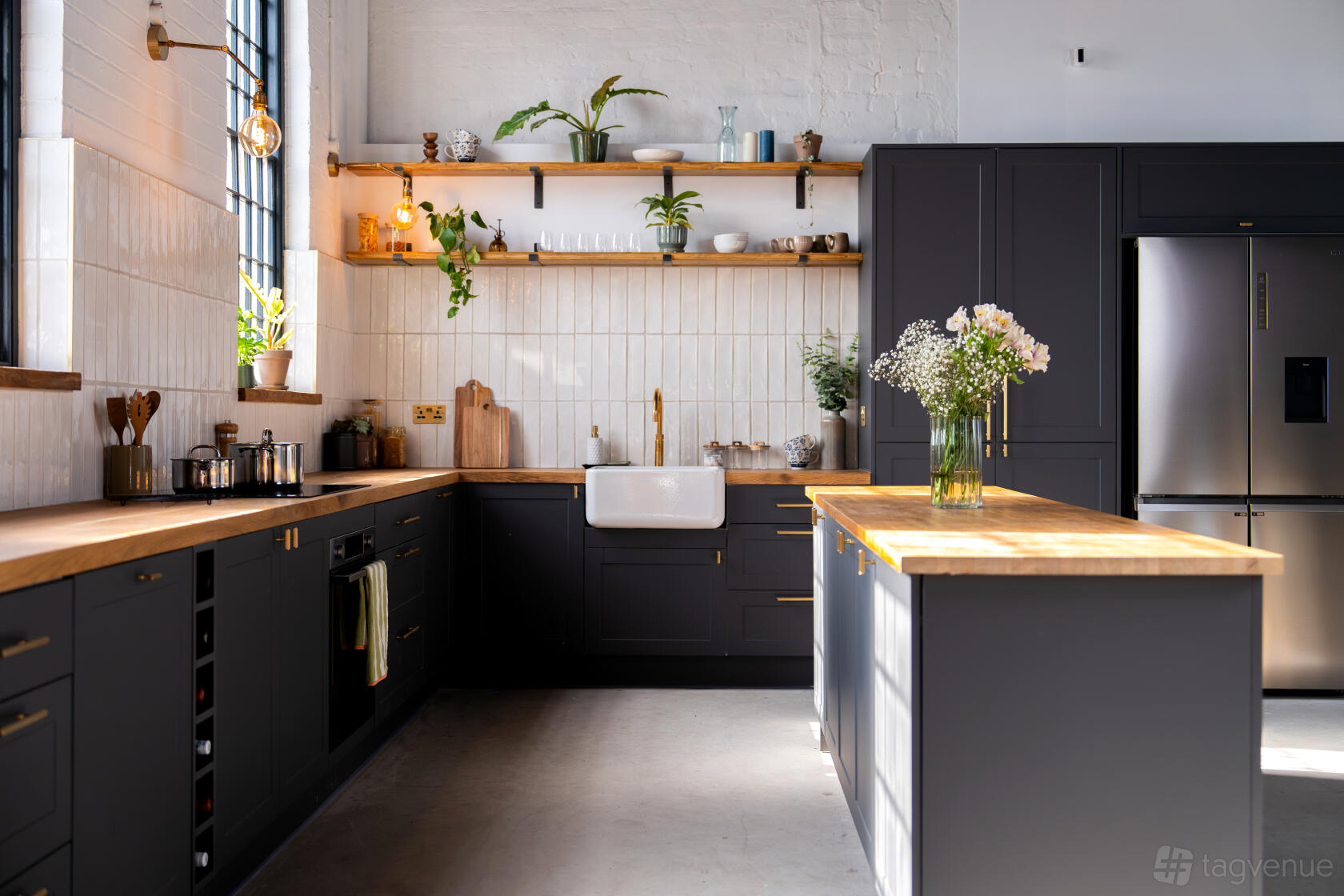 A kitchen set with dark cabinetry, wooden countertops, open shelves with plants, and a farmhouse sink at Flux Studio.