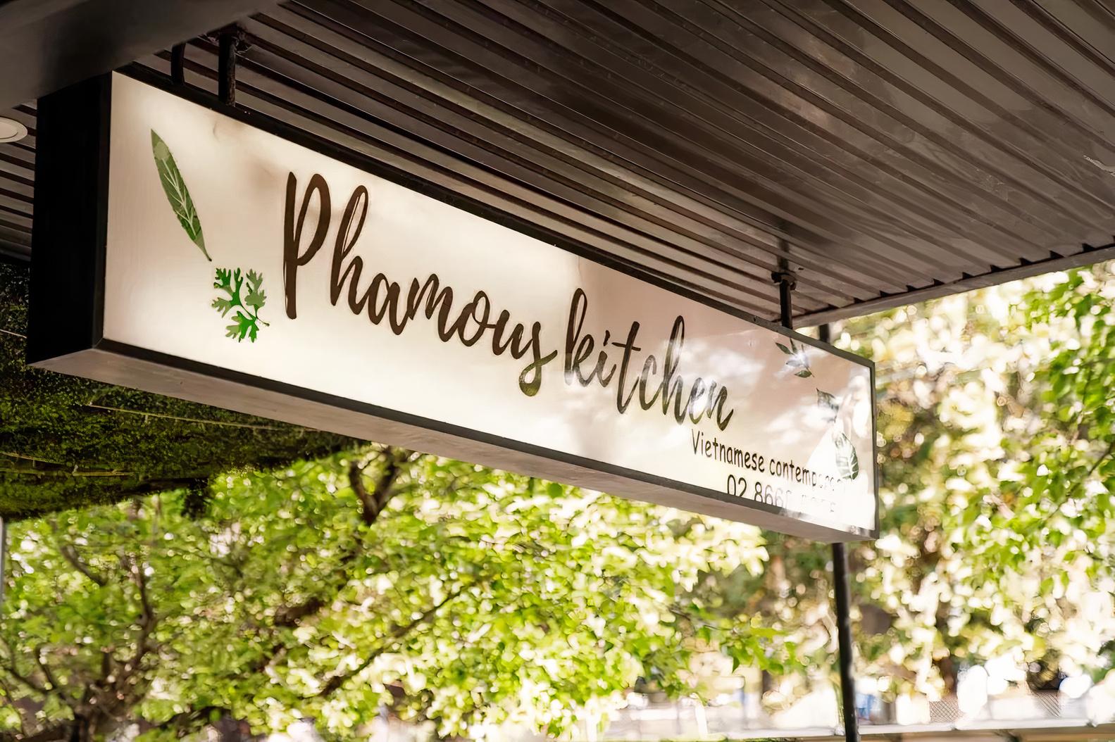 A restaurant sign with greenery and trees visible behind it at Phamous Kitchen.