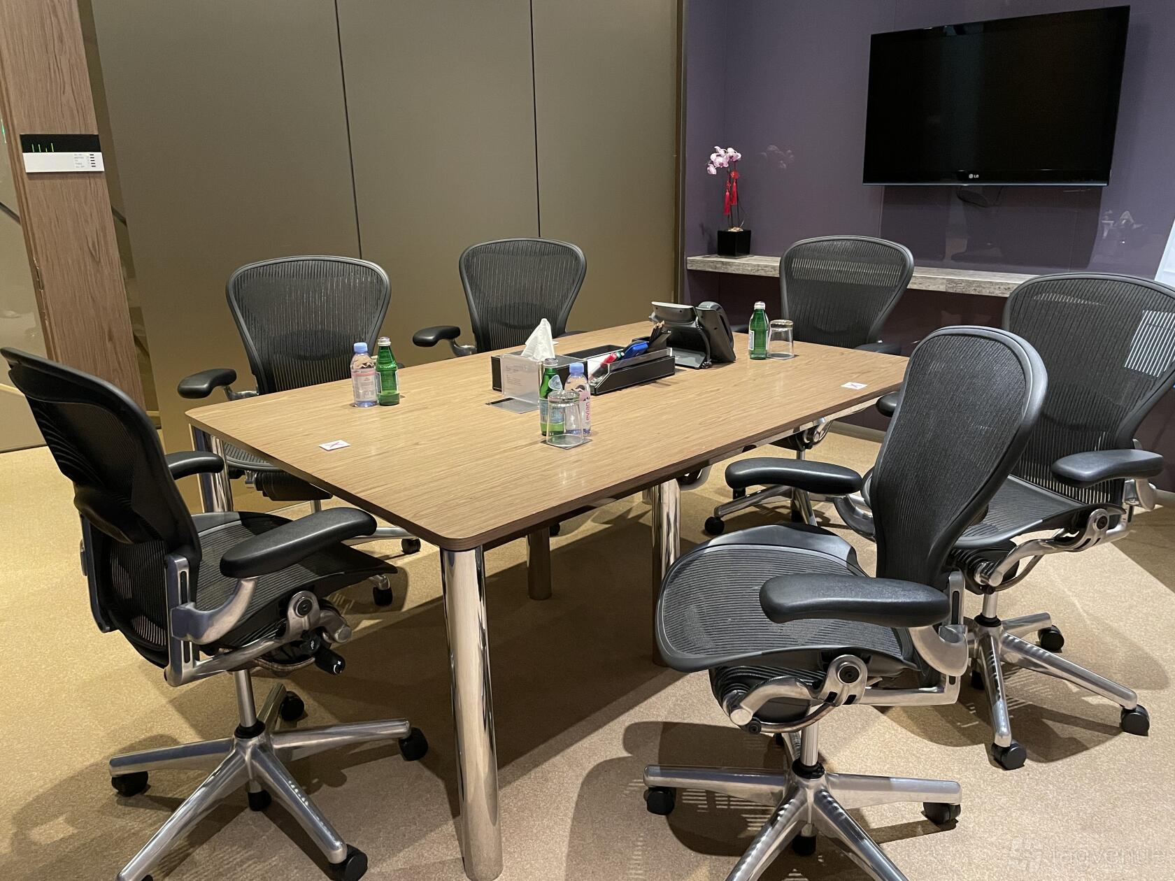 A meeting room with a rectangular wooden table, six mesh office chairs, bottled water, and a wall-mounted screen at Ocean Financial Centre.