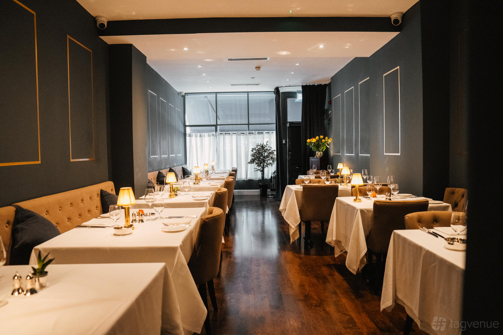 A function room in a restaurant with white tablecloths, upholstered seating, and dim accent lighting at Jamuna.