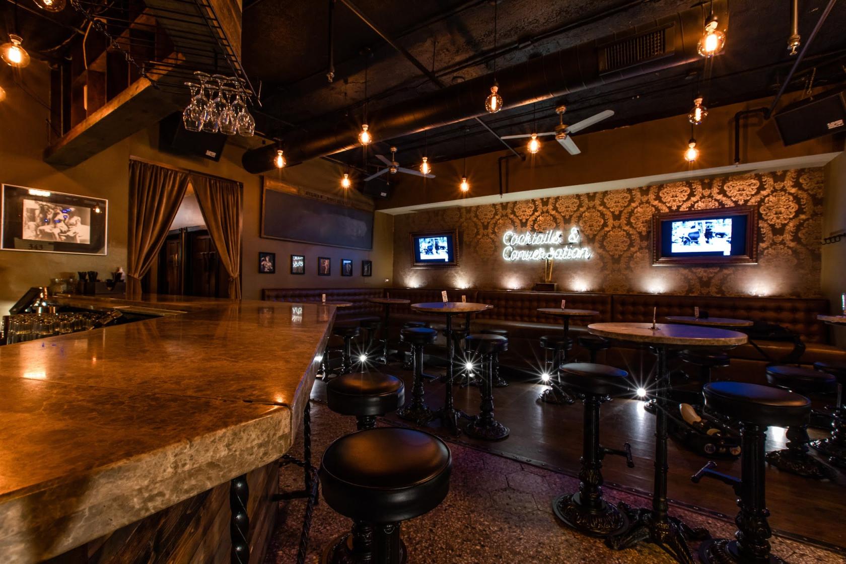 An event space in a bar with exposed bulb lighting, patterned wallpaper, and a neon sign at Brandos in the Loop.