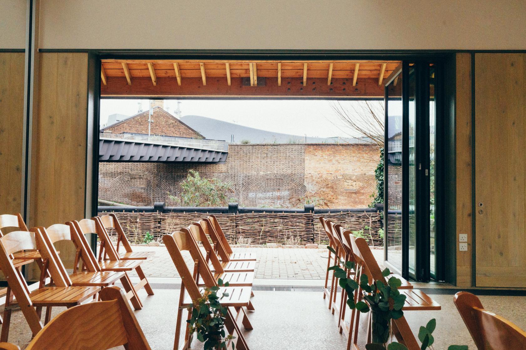 An event venue with folding wooden chairs and floor-to-ceiling glass doors opening to an outdoor courtyard at Camley Street Natural Park.