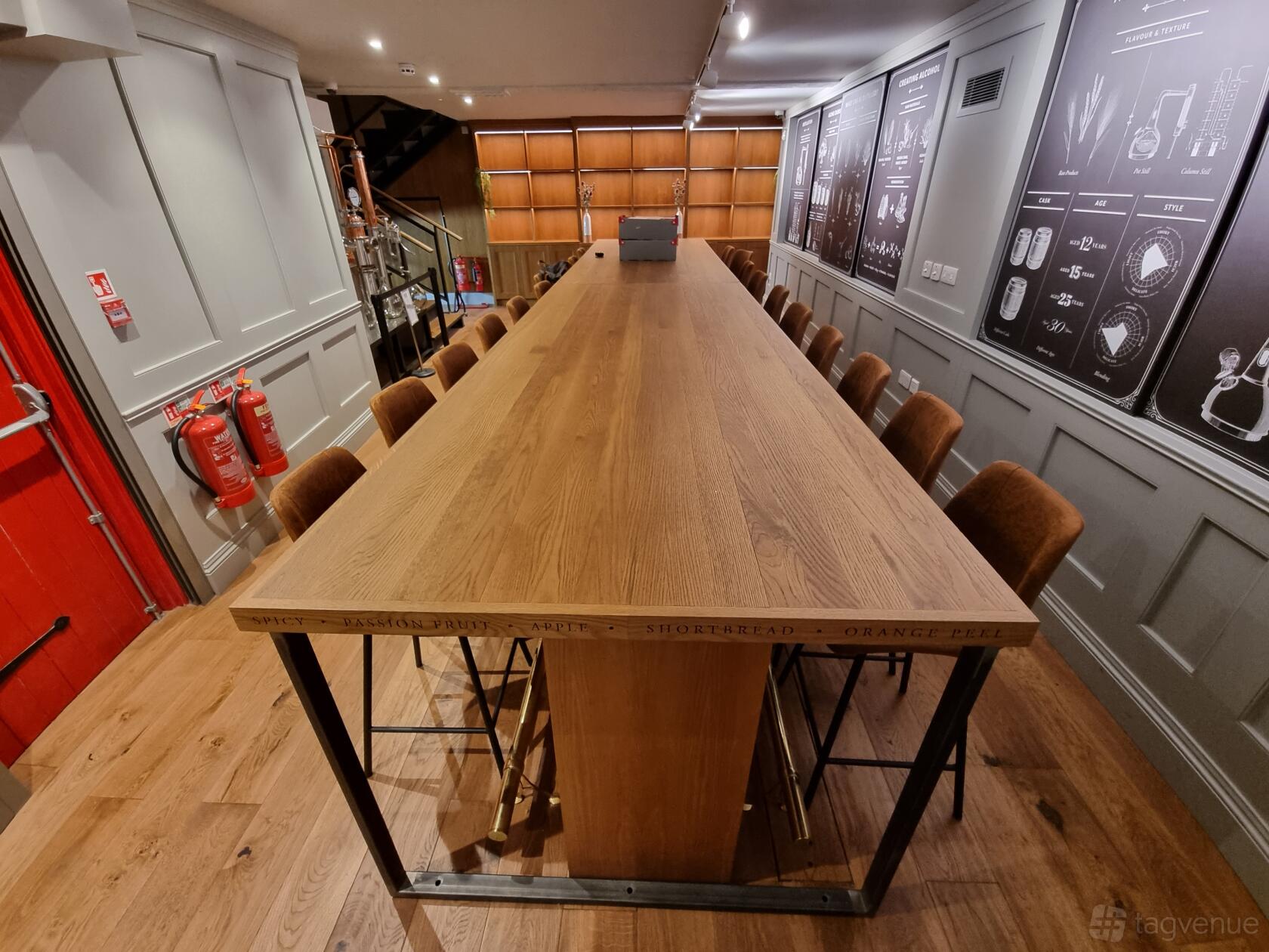 A bar with a long wooden communal table, high-back chairs, and illustrated wall panels at London Bridge Distillery School.