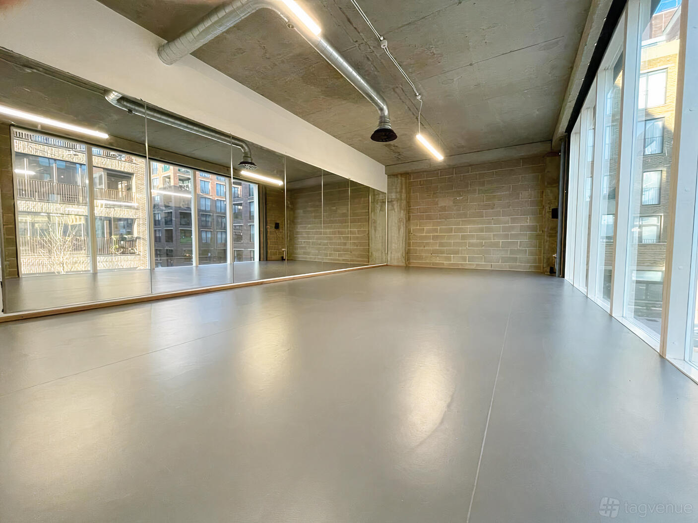An art studio with floor-to-ceiling mirrors, concrete ceiling, large windows, and exposed ducts at Create Destroy Studios.