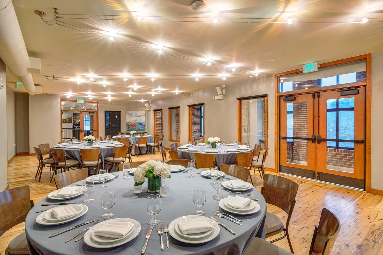 A ballroom in a restaurant with round tables draped in gray linens, wooden chairs, and wall art at Pinstripes - Georgetown DC.