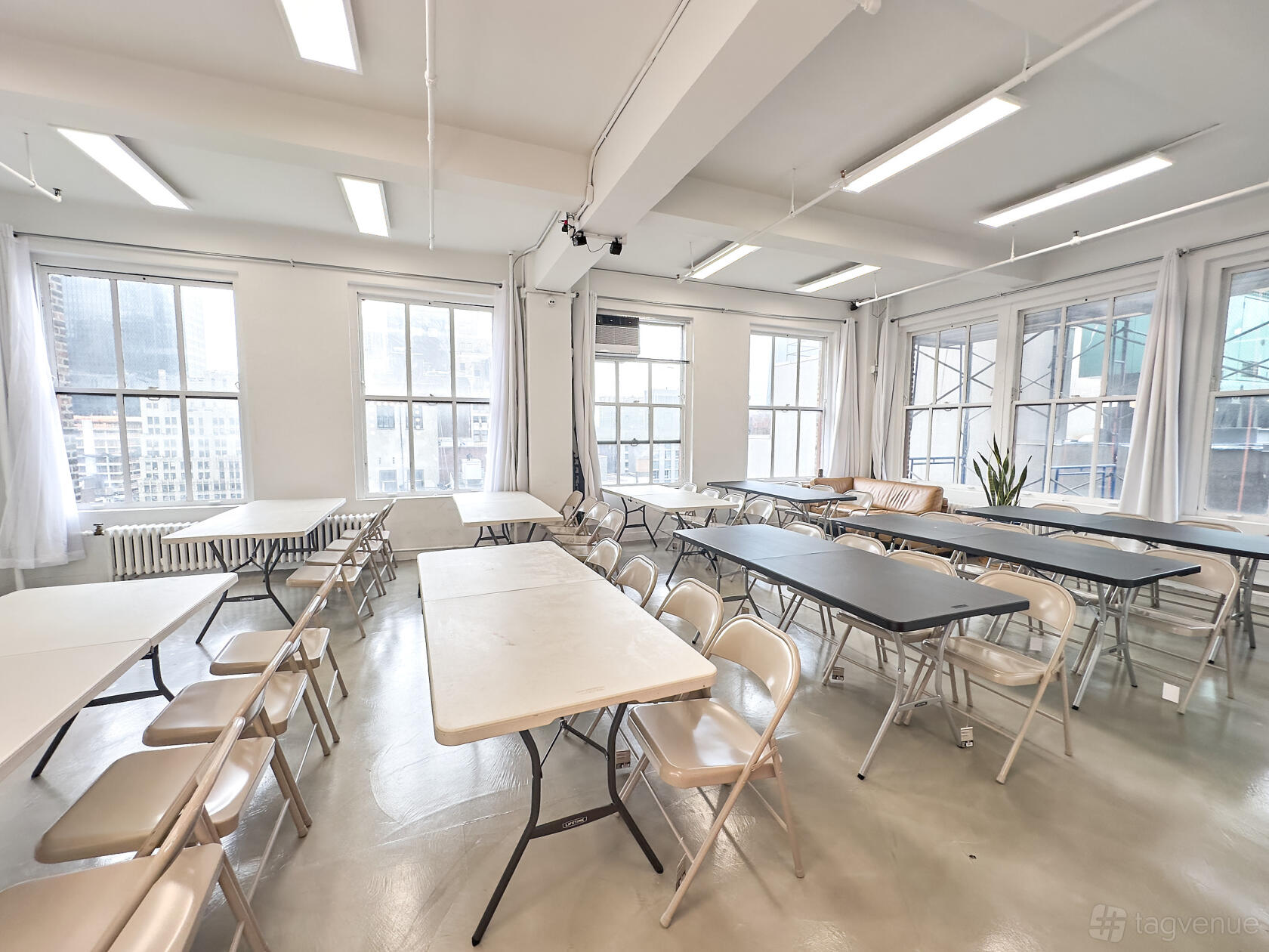 An event space in a loft with large windows, white walls, folding tables, and natural light at Event Rental Space Manhattan 23rd Floor.
