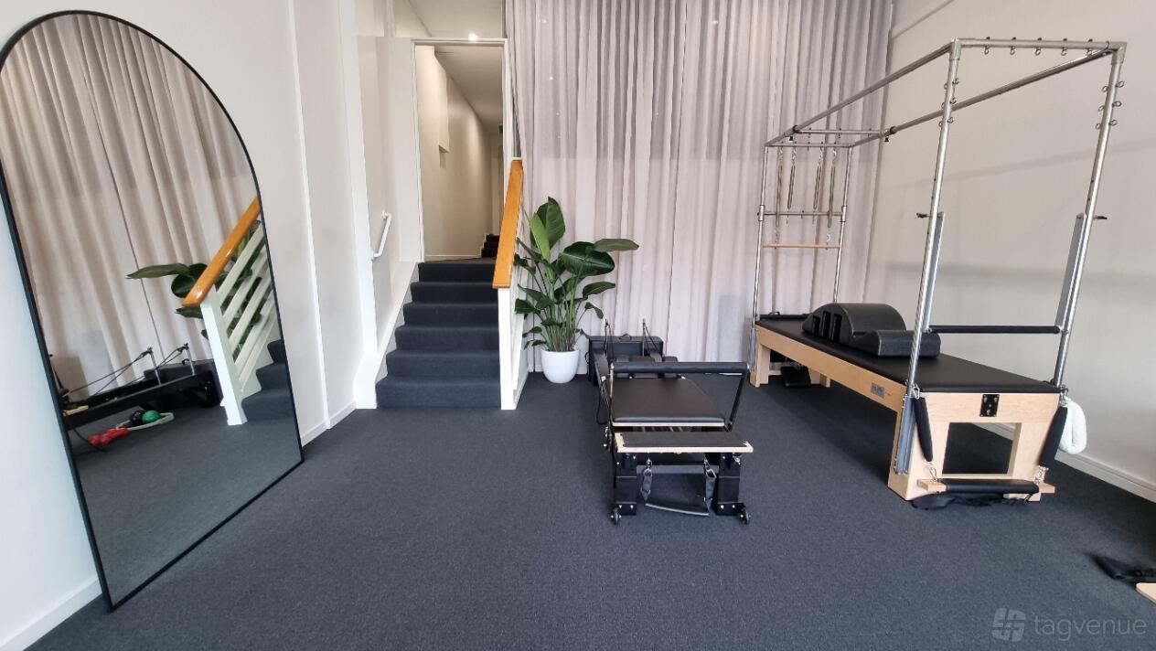 A pilates studio with a reformer machine, large wall mirror, potted plant, and carpeted floor at Foundation Health.