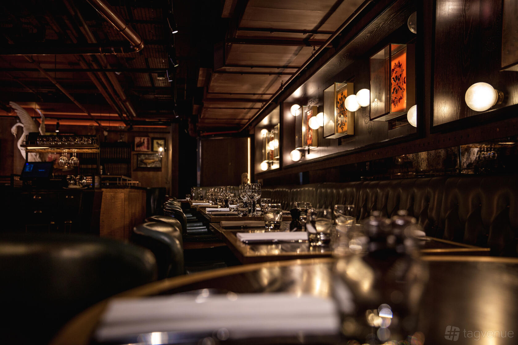 An event space in a restaurant with dark leather banquette seating, globe wall lights, and framed artwork at The Botanist Broadgate Circle.