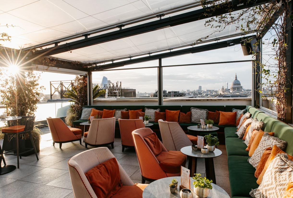 A rooftop lounge with cushioned seating, orange and green accents, and city skyline views at Wagtail.