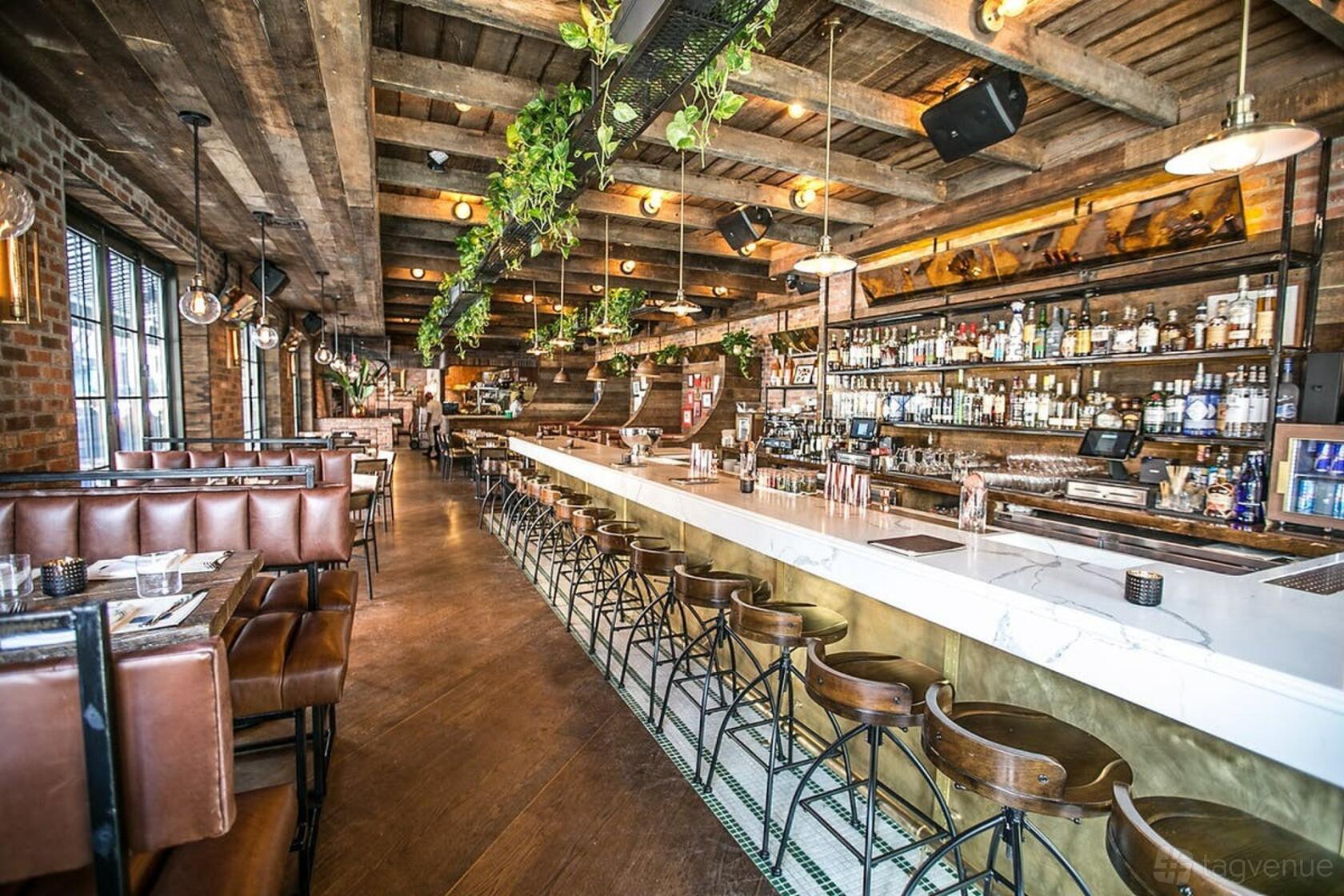A restaurant with a long marble bar, leather banquettes, exposed brick, and wood beam ceilings at Loulou Petit Bistro & Speakeasy.