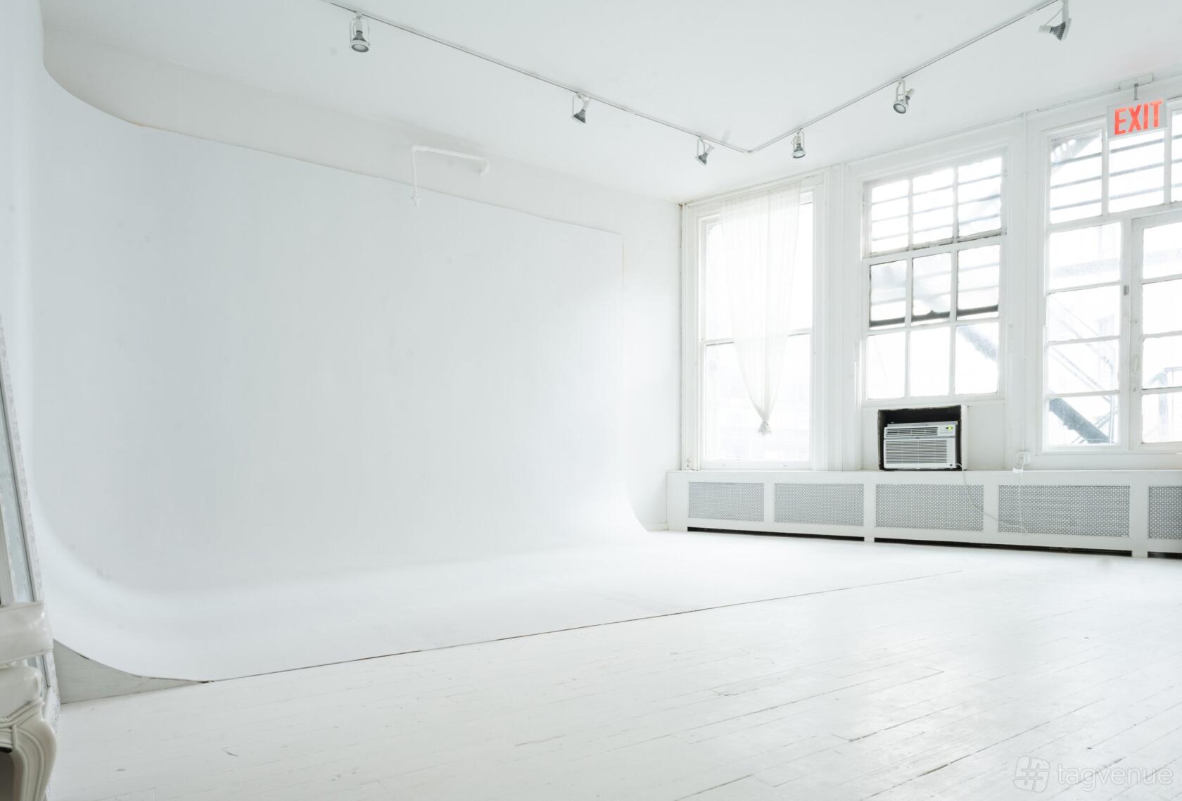 A photo studio with a white cyclorama wall, white wooden floors, and tall windows at LeVue Studios.