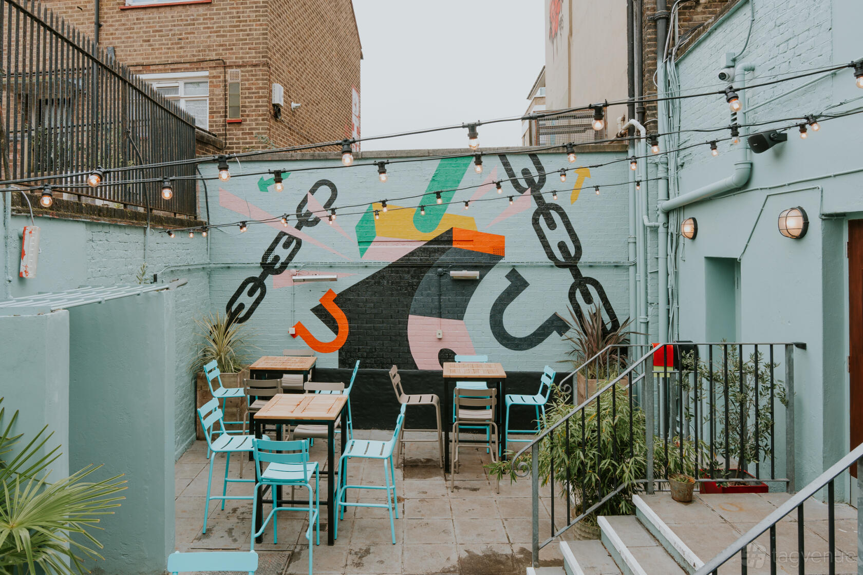 An outdoor pub garden with string lights, colorful mural, and turquoise chairs at Hawkins Forge.
