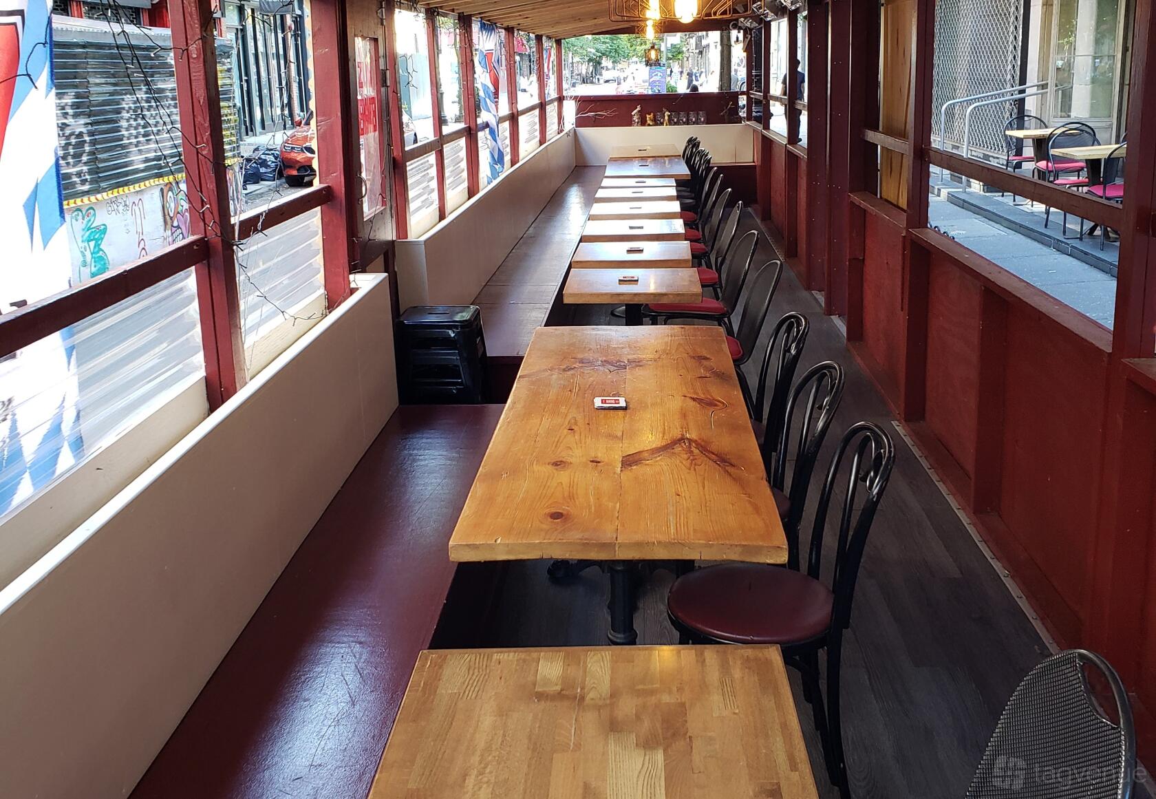An outdoor dining area with long wooden tables, black chairs, and bench seating at Cafe Katja