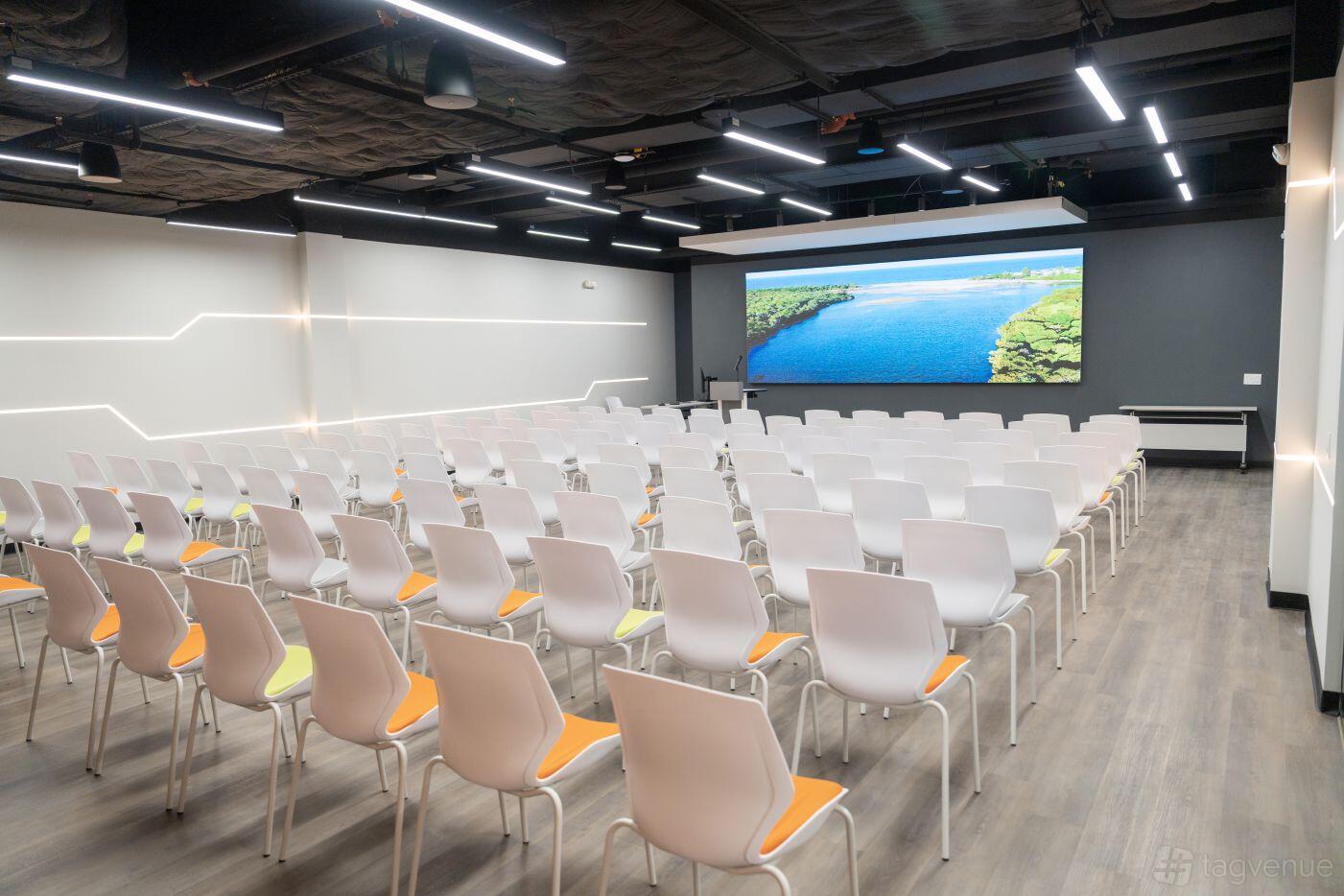 An auditorium with rows of white chairs, wood flooring, and a large digital screen at LaunchHub Space.