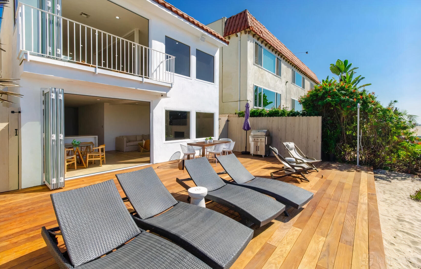 A beachfront penthouse with wicker lounge chairs on a wooden deck and open patio doors at Modern Boho Beach House.