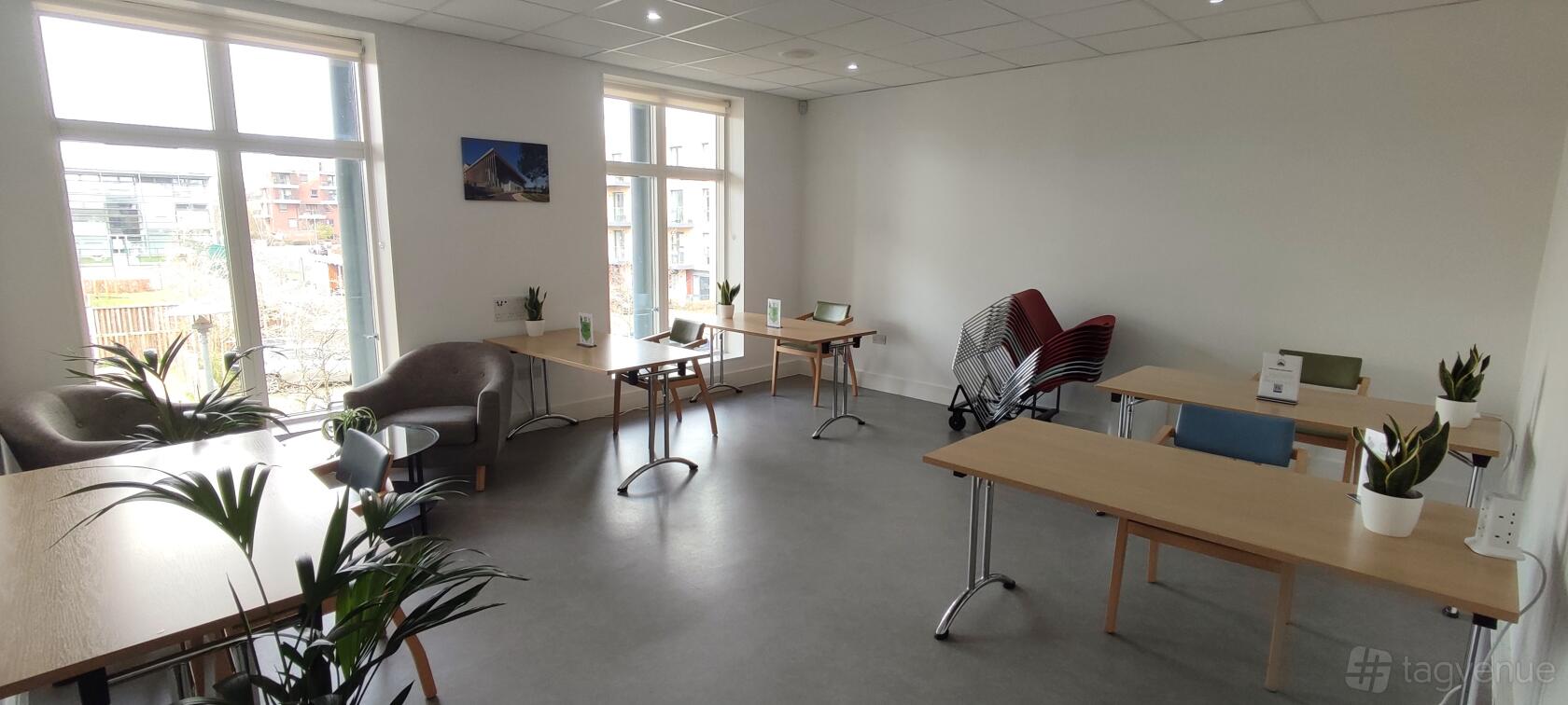 An office space with natural light, simple wooden tables, and chairs stacked in the corner at OneStonegrove.