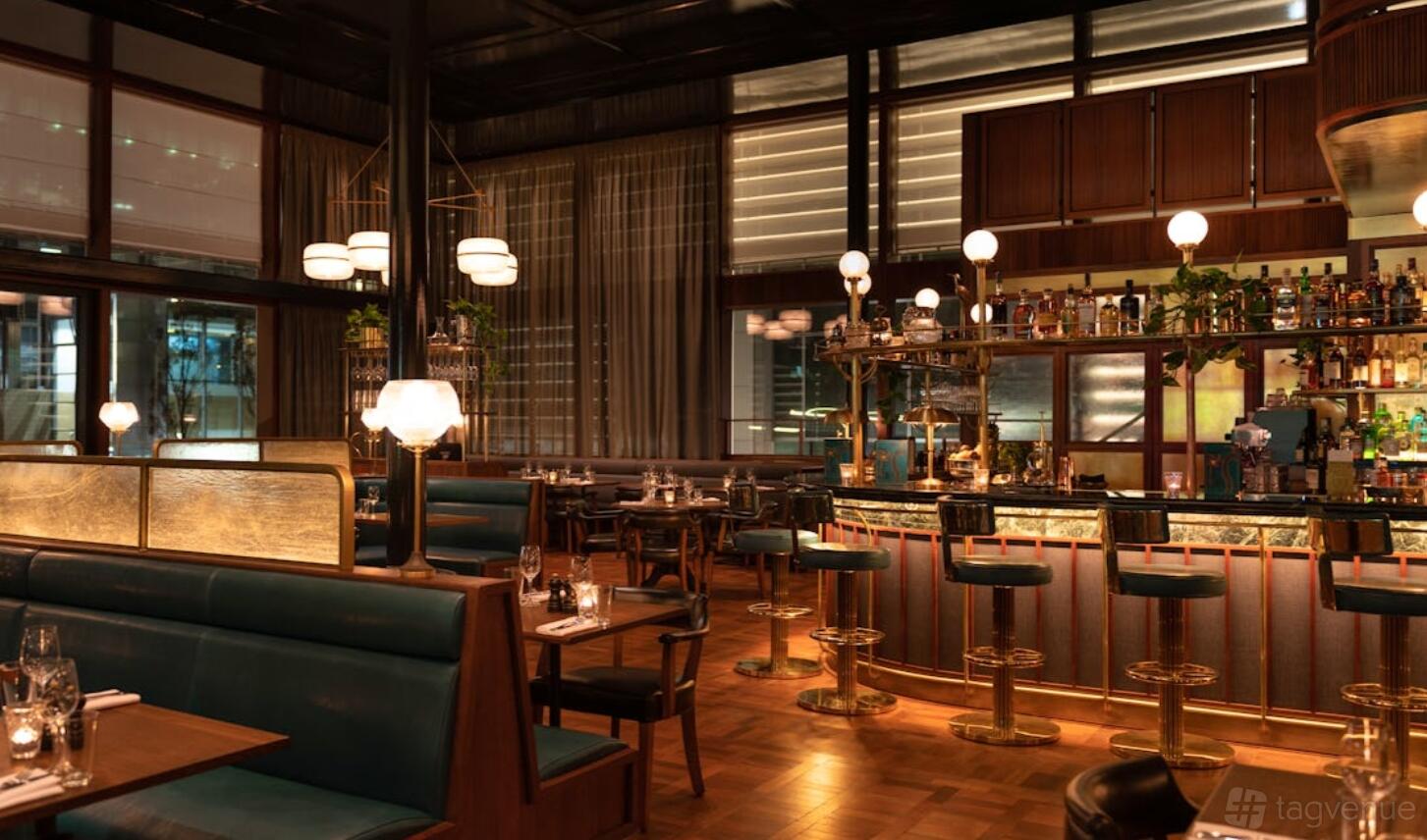 A restaurant with teal leather booths, round globe lamps, and a brass-accented bar at Hawksmoor Wood Wharf.