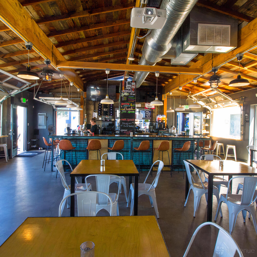 A bar in a restaurant with exposed wood beams, teal-tiled bar front, and metal chairs at 619 Spirits North Park.