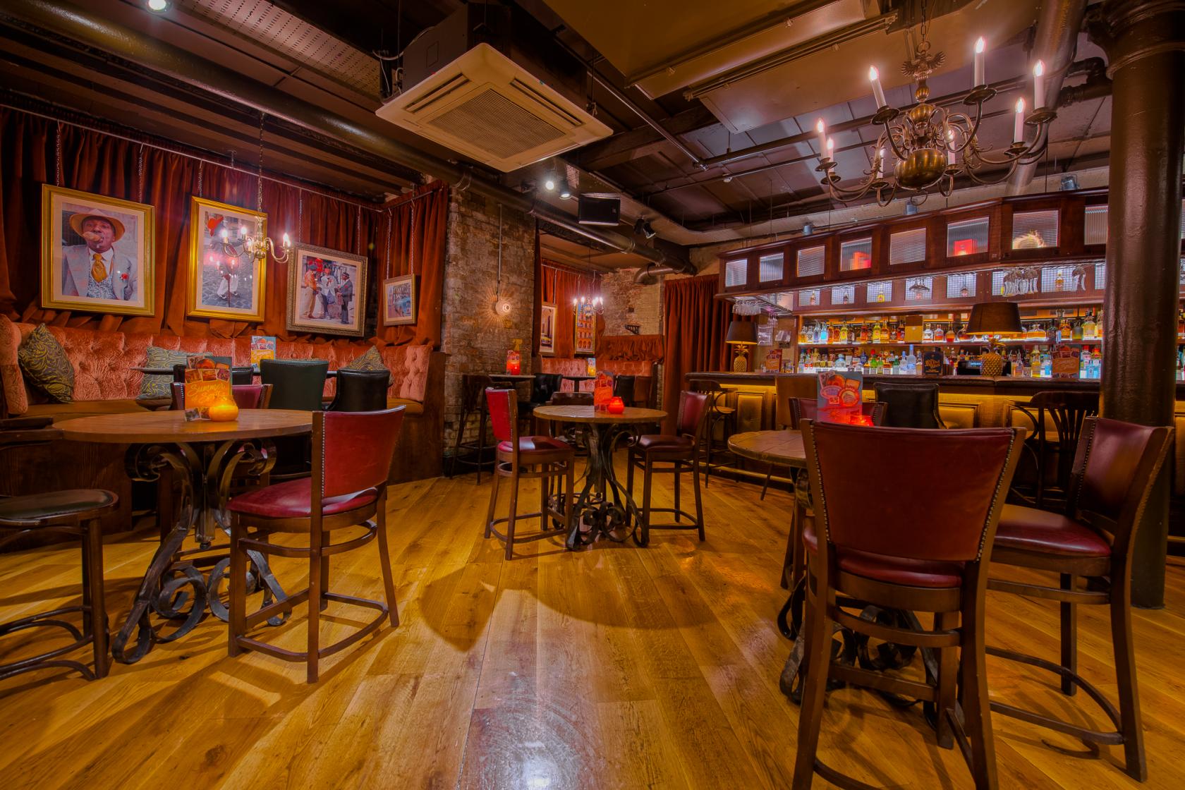 An event space in a restaurant with wooden floors, exposed brick, red velvet seating, and a backlit bar at Revolución de Cuba Manchester.