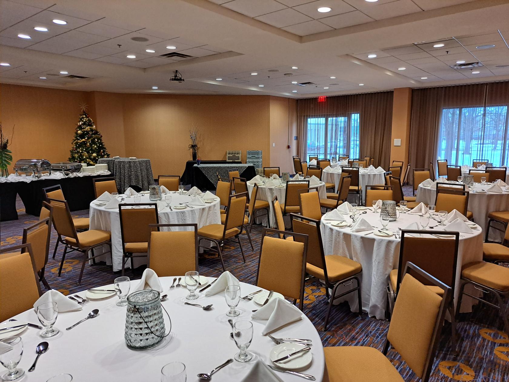 An event space with round tables dressed in white linens, set with glassware and napkins at TownePlace Suites Toronto Northeast/Markham.
