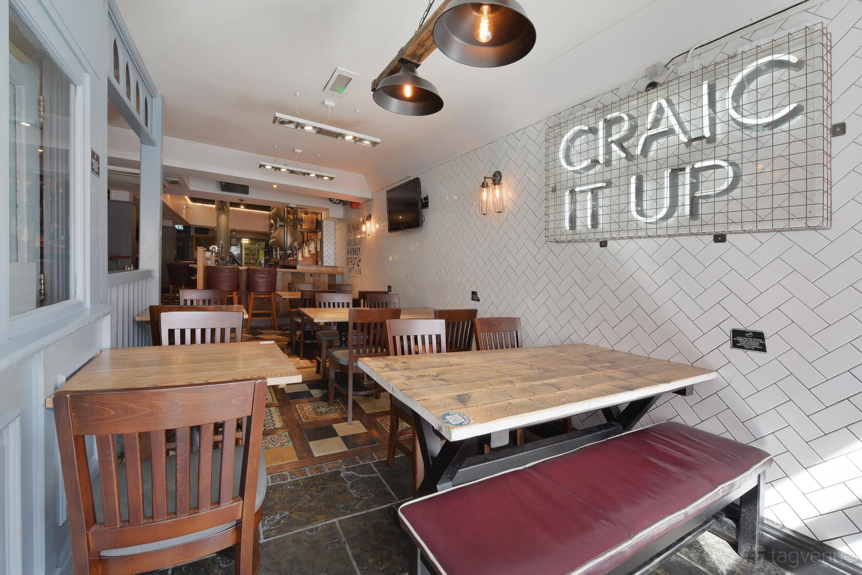 A pub interior with wooden tables and chairs, tiled floor, and a neon 'Craic It Up' sign at O'Neill's Wardour Street.
