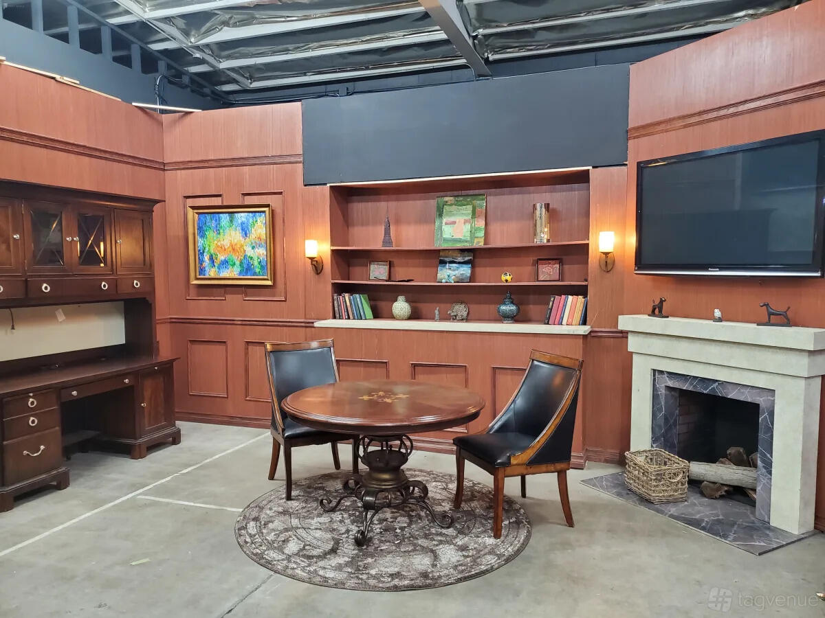 A photo studio with wood-paneled walls, a round table, bookshelves, and a fireplace at Cosmic Cube Creative Studio.