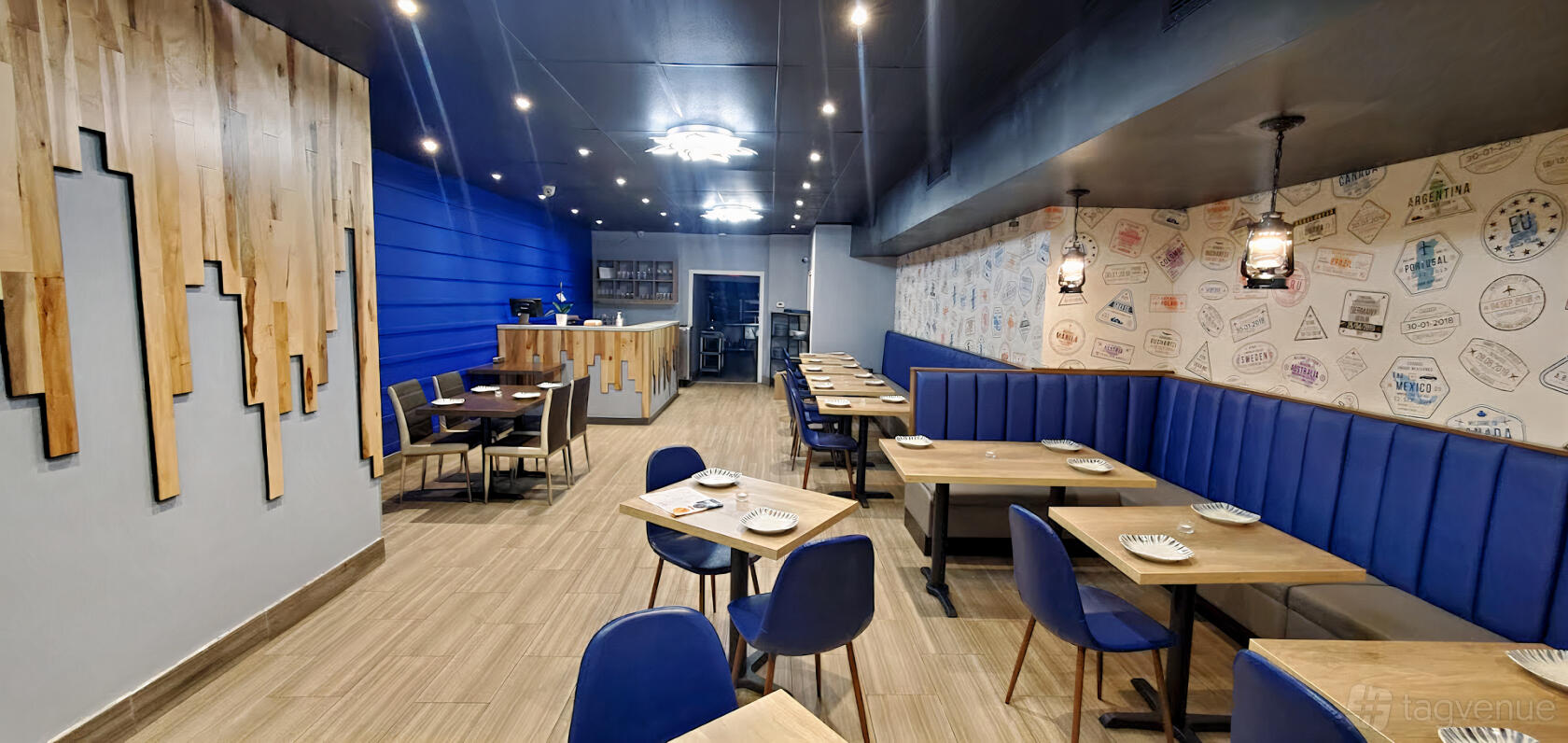 A dining area with blue banquette seating, wooden tables, patterned accent wall, and pendant lighting at Raahi Modern Indian Kitchen & Bar.
