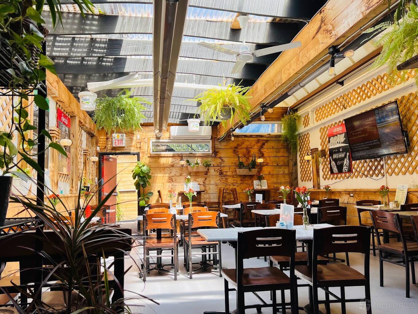 A covered terrace with natural wood walls, hanging plants, and ceiling fans at Utopia Cafe & Grill.