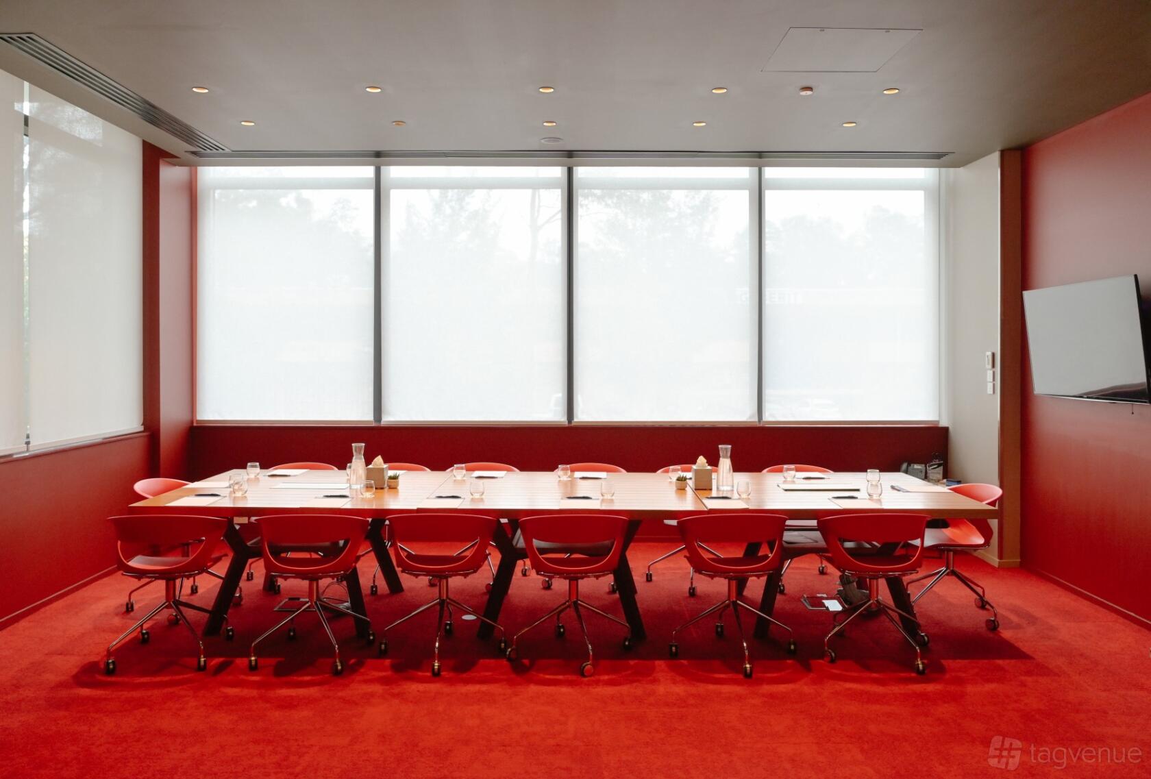 A meeting room with red carpet, red chairs around a rectangular table, large windows, and a wall-mounted TV at Holiday Inn Express Sydney Macquarie Park.
