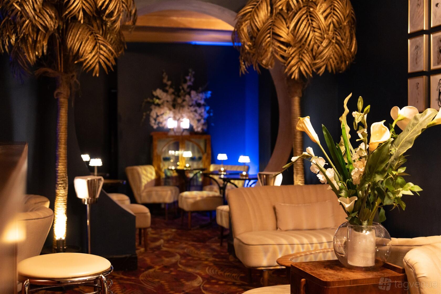 A bar with gold palm tree decor, plush cream seating, floral arrangements, and ambient lighting at Fontaine's Bar.
