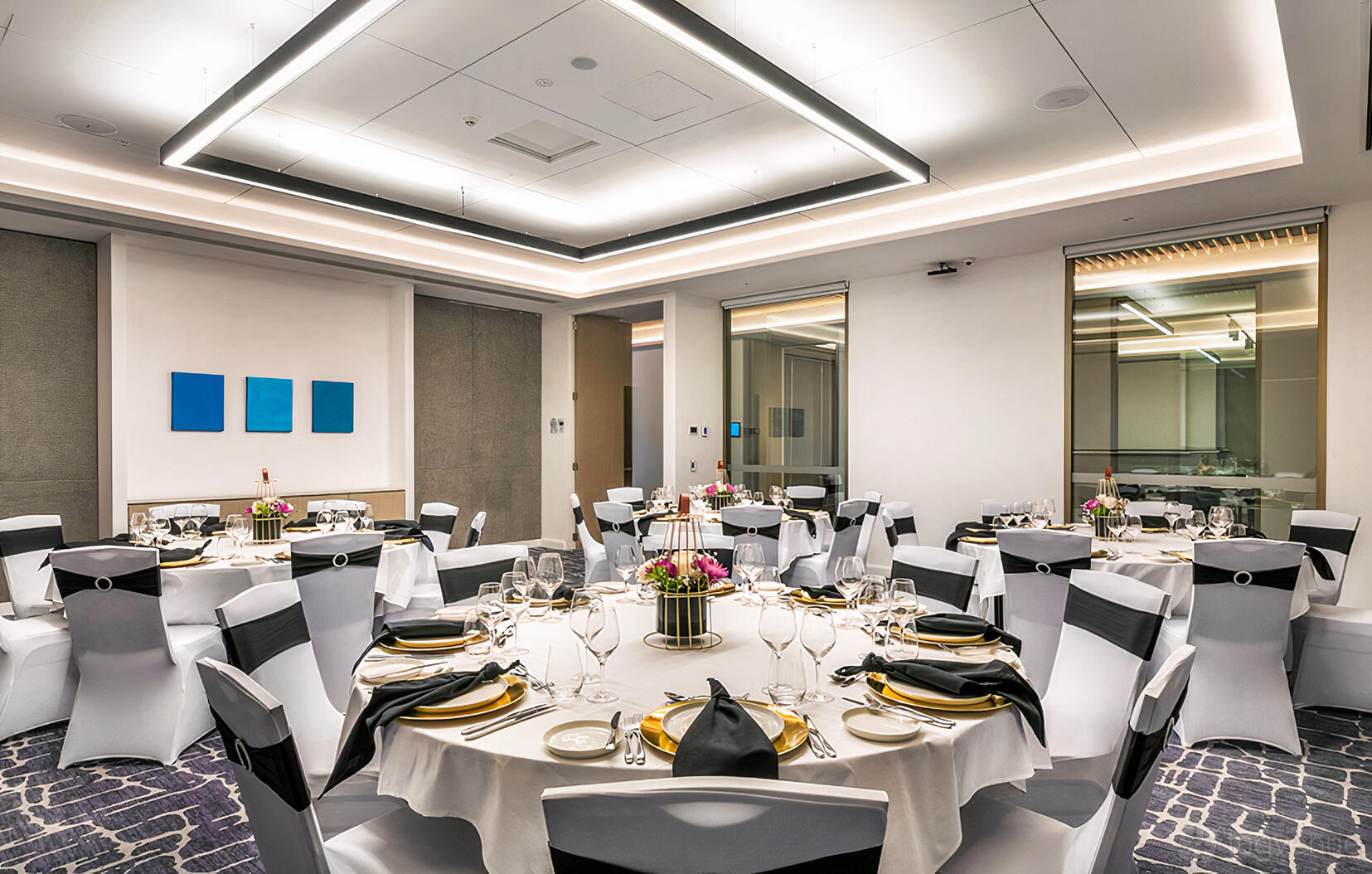 A hotel hall with round tables set with white linens, banquet chairs, and floral centerpieces at Crowne Plaza Sydney Coogee Beach.
