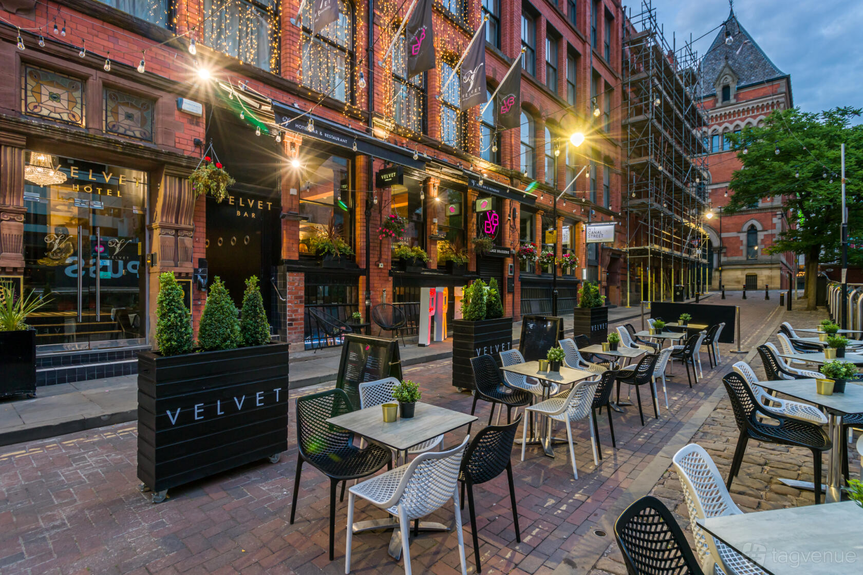 An outdoor hotel terrace with bistro tables, black planters, and string lights at Velvet Hotel, Bar & Brasserie.