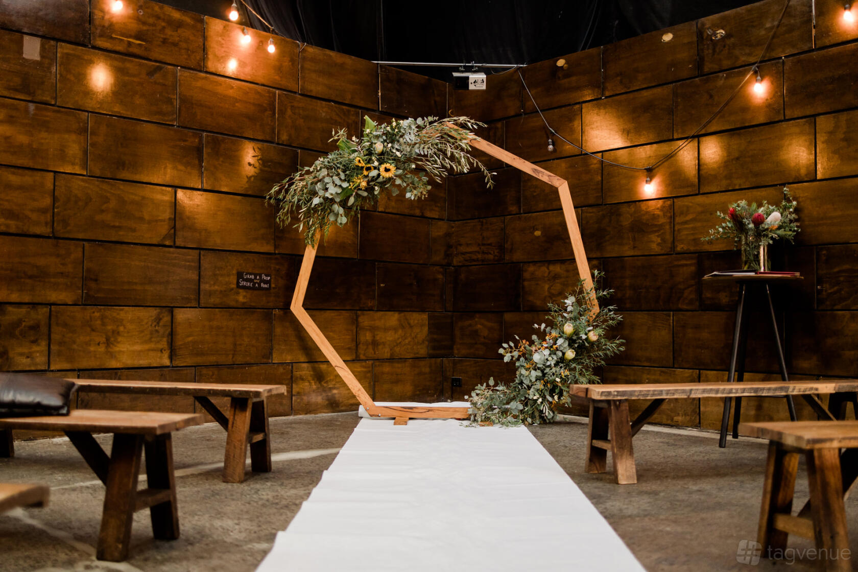 An event venue with wooden panel walls, hanging string lights, and a hexagonal floral arch at Rokeby 100.