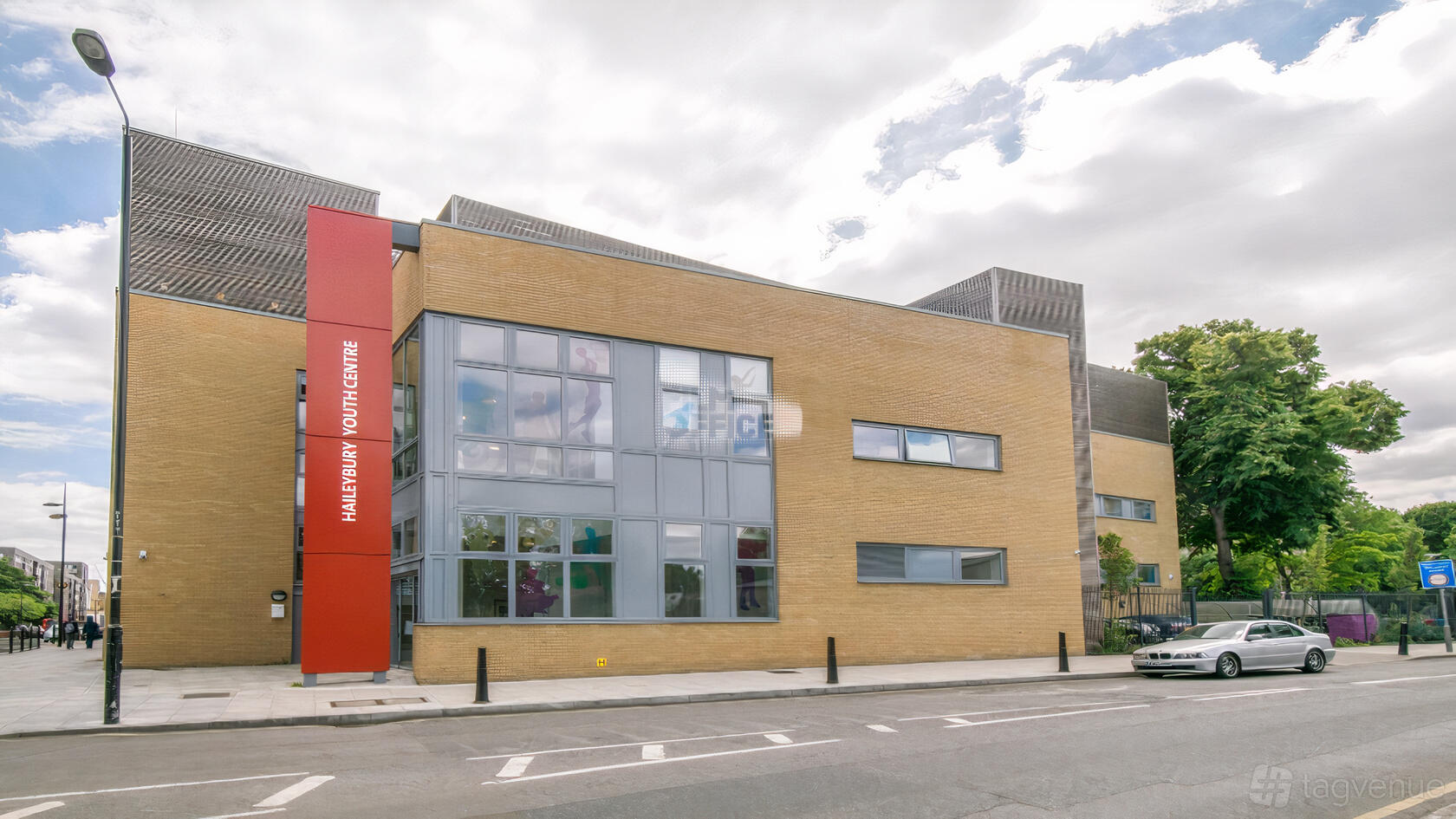A versatile event space with large windows and a bold red vertical sign on the brick facade at Haileybury Sports and Events Centre.