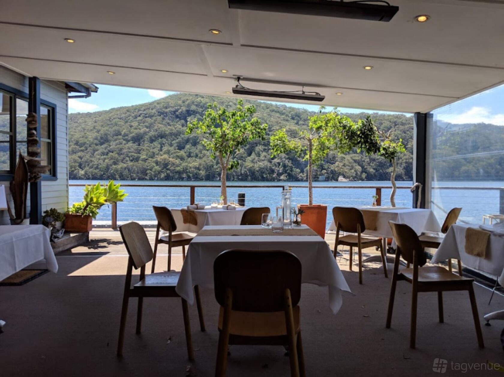 A waterfront restaurant with floor-to-ceiling windows, white tablecloths, and views of the river at Cottage Point Inn.