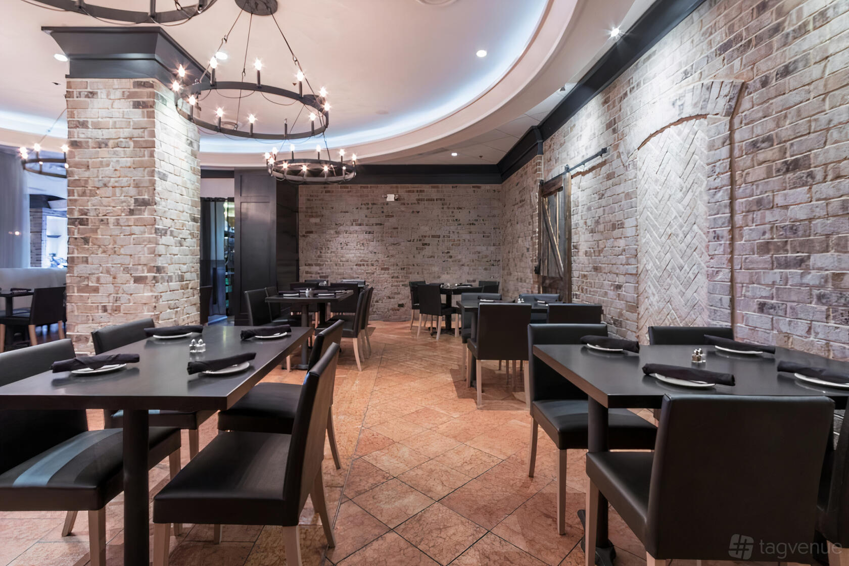 A restaurant with exposed brick walls, round chandeliers, and black dining tables at Rivers Restaurant.