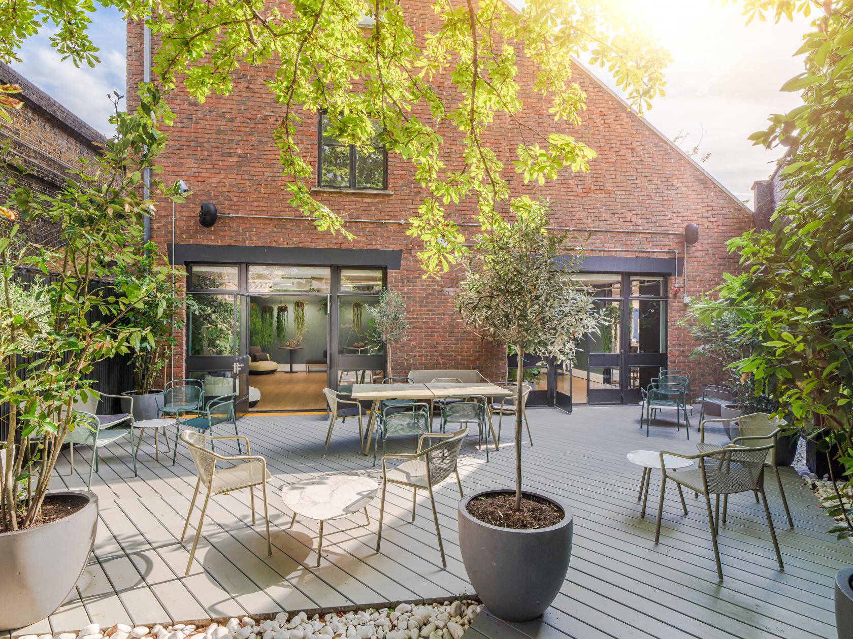 An outdoor meeting space with potted trees, modern patio furniture, and a wooden deck at Uncommon Fulham.