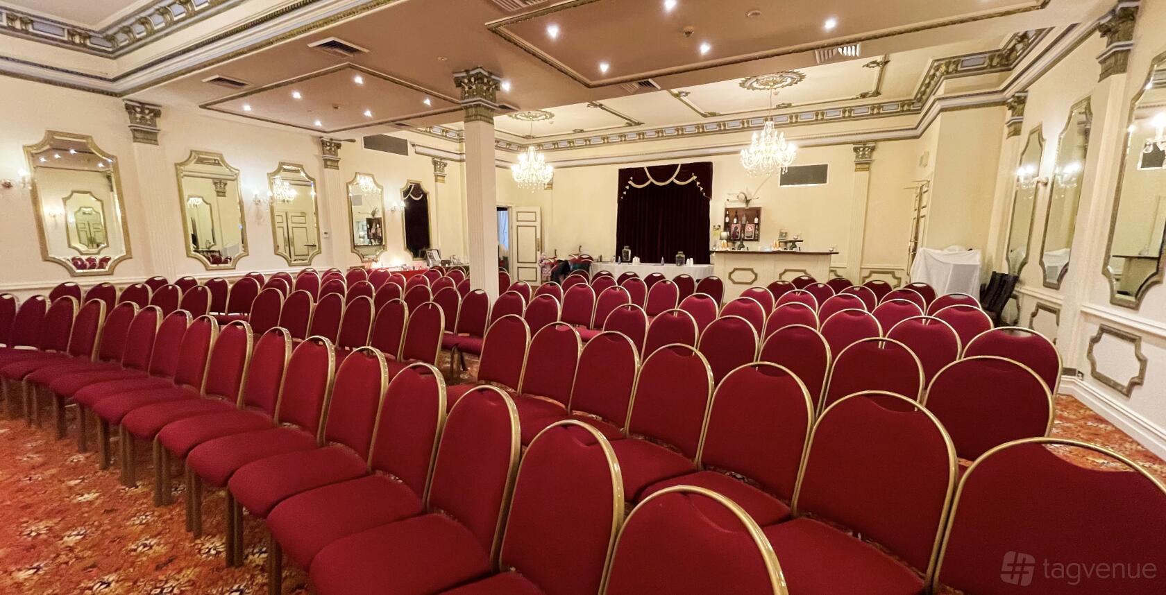 A ballroom with rows of red cushioned chairs, chandeliers, and ornate mirrors at Palais Royale Boutique Hotel.