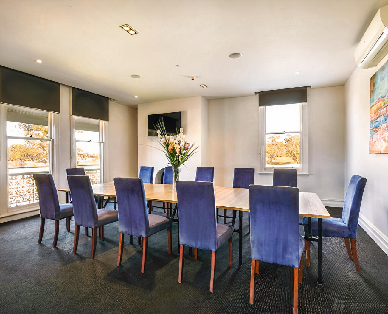 A meeting room with a long wooden table, blue upholstered chairs, large windows, and a vase of flowers at The Bridge Inn Hotel.
