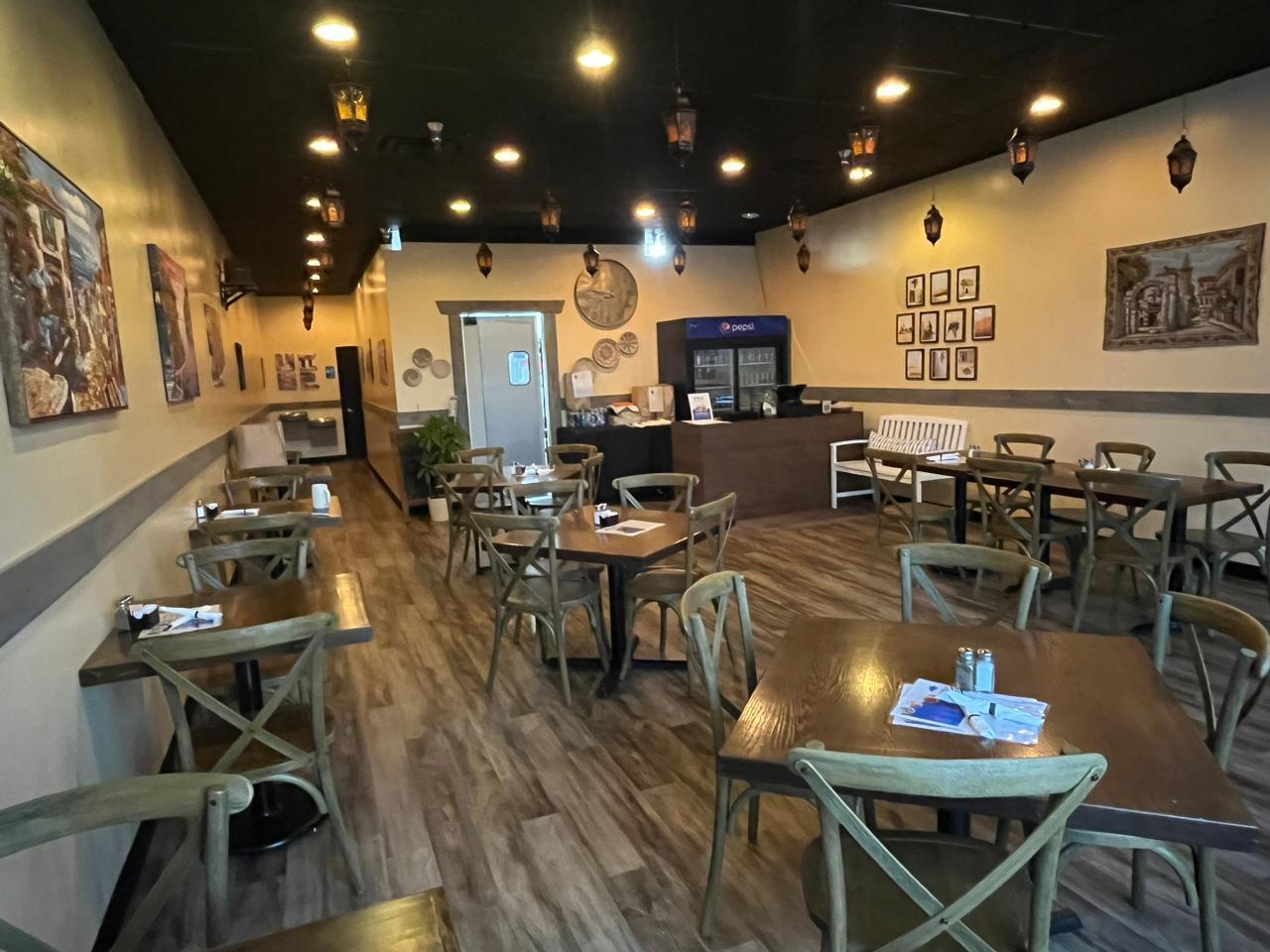 A restaurant with wooden tables, cross-back chairs, Middle Eastern decor, and pendant lanterns at Byblos Express Greek and Lebanese Greenwood.