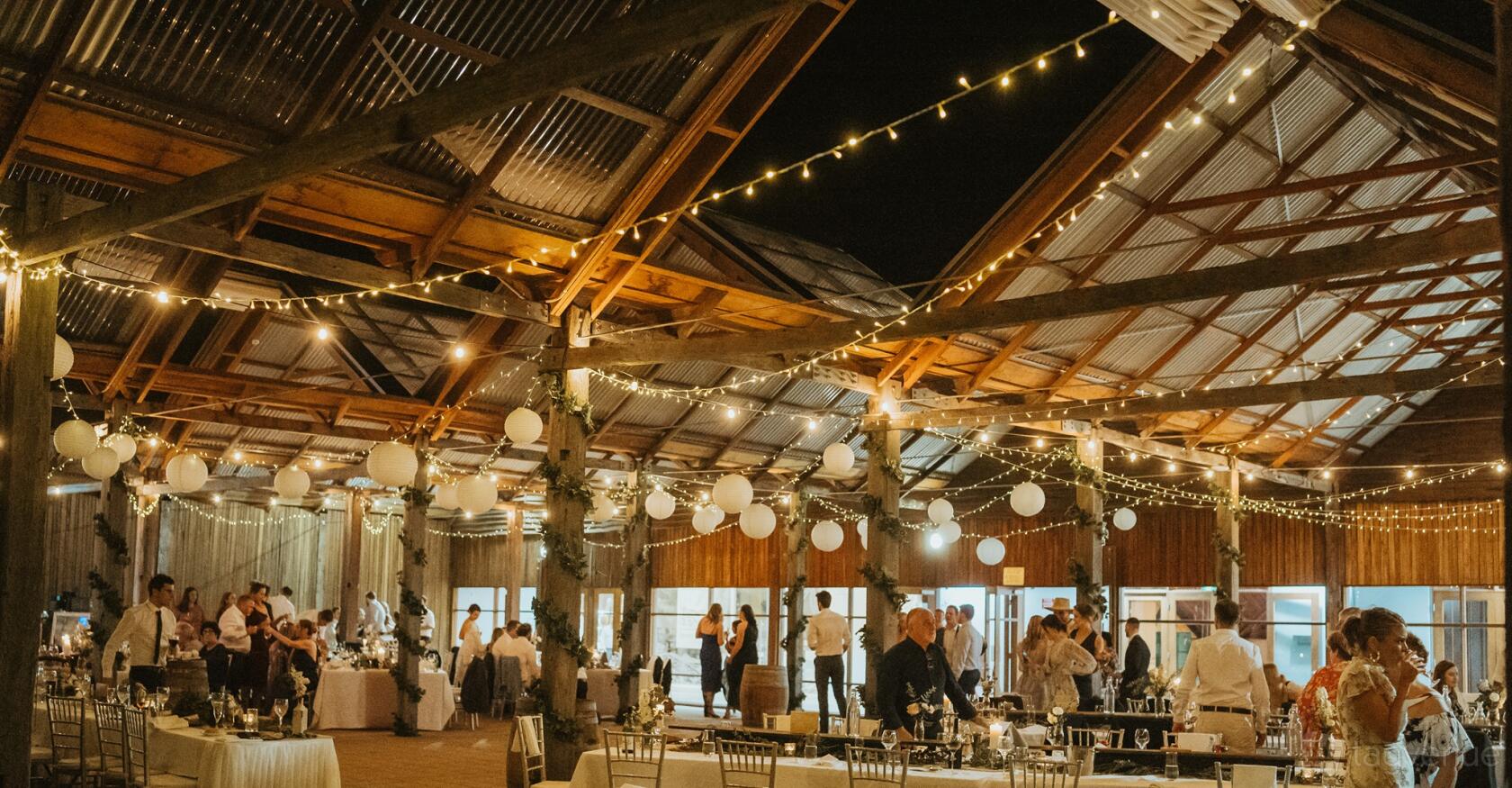A barn with exposed timber beams, string lights, hanging paper lanterns, and banquet tables at Ben Ean Estate.