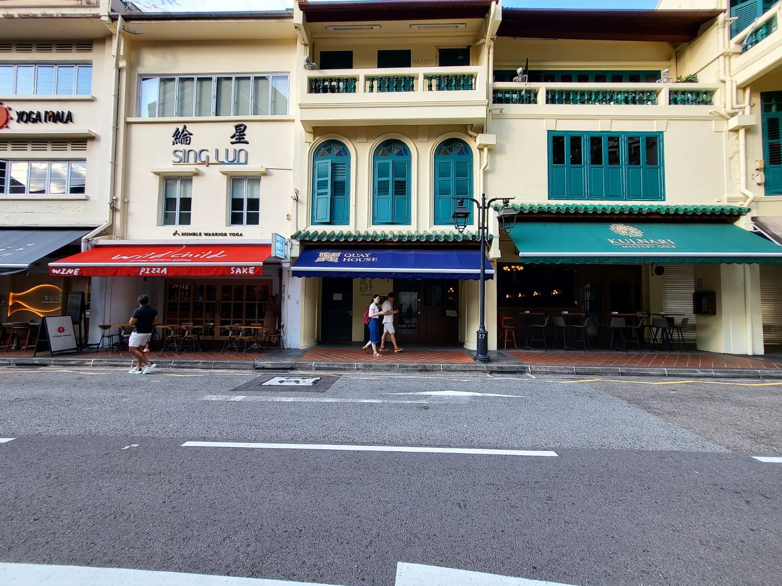 A restaurant with a dark blue awning, large windows, and outdoor seating at Quay House.