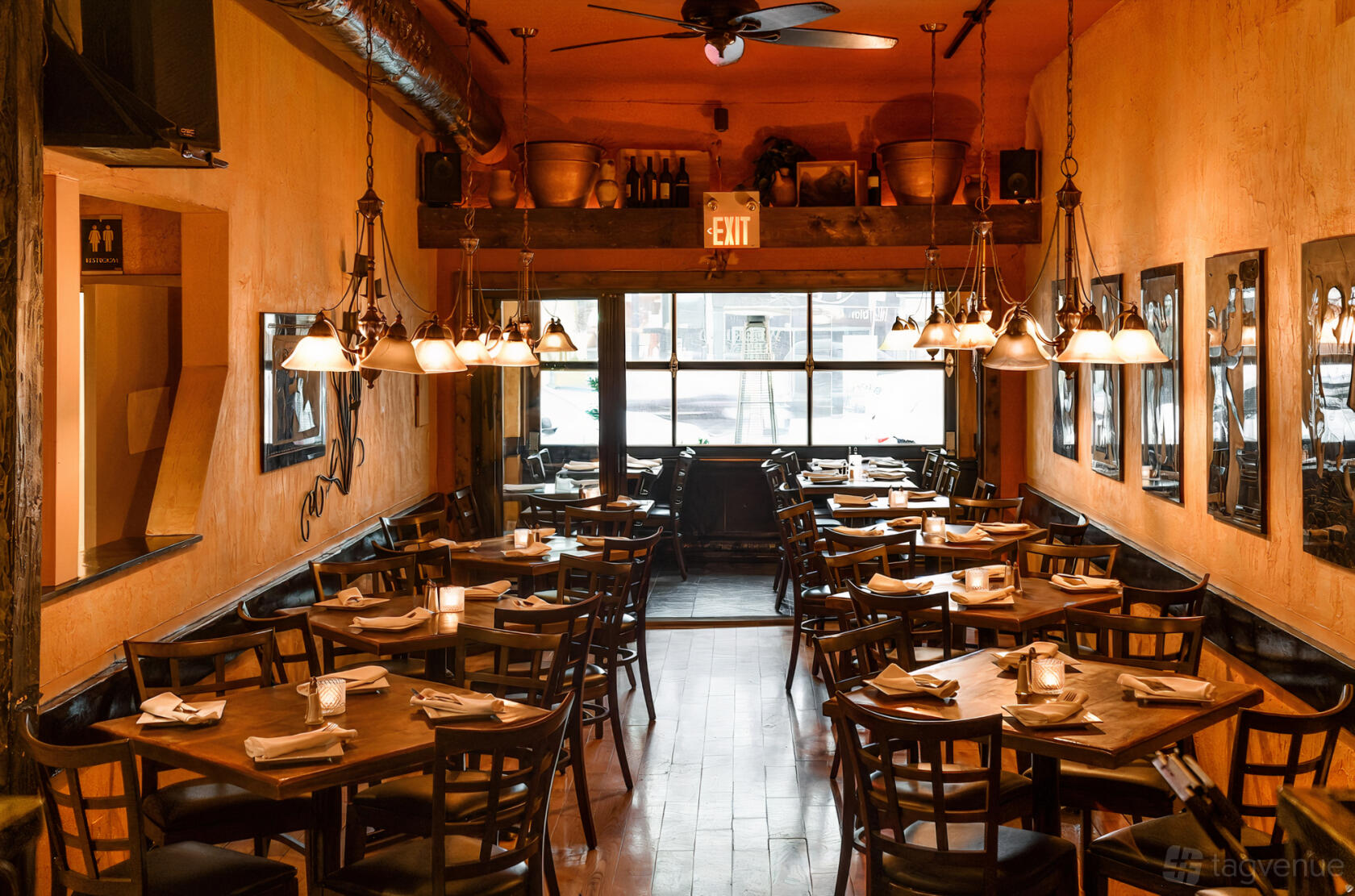 A restaurant dining area with warm lighting, wooden tables set with white napkins, and wall art at Christina's on the Danforth.