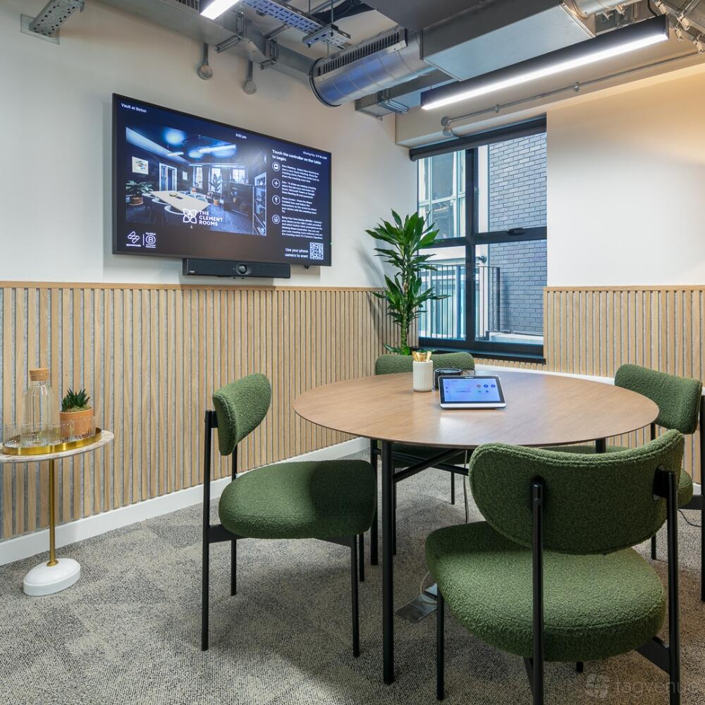 A meeting room with a round table, green chairs, wall-mounted screen, and large window at Spacemade - Beton.