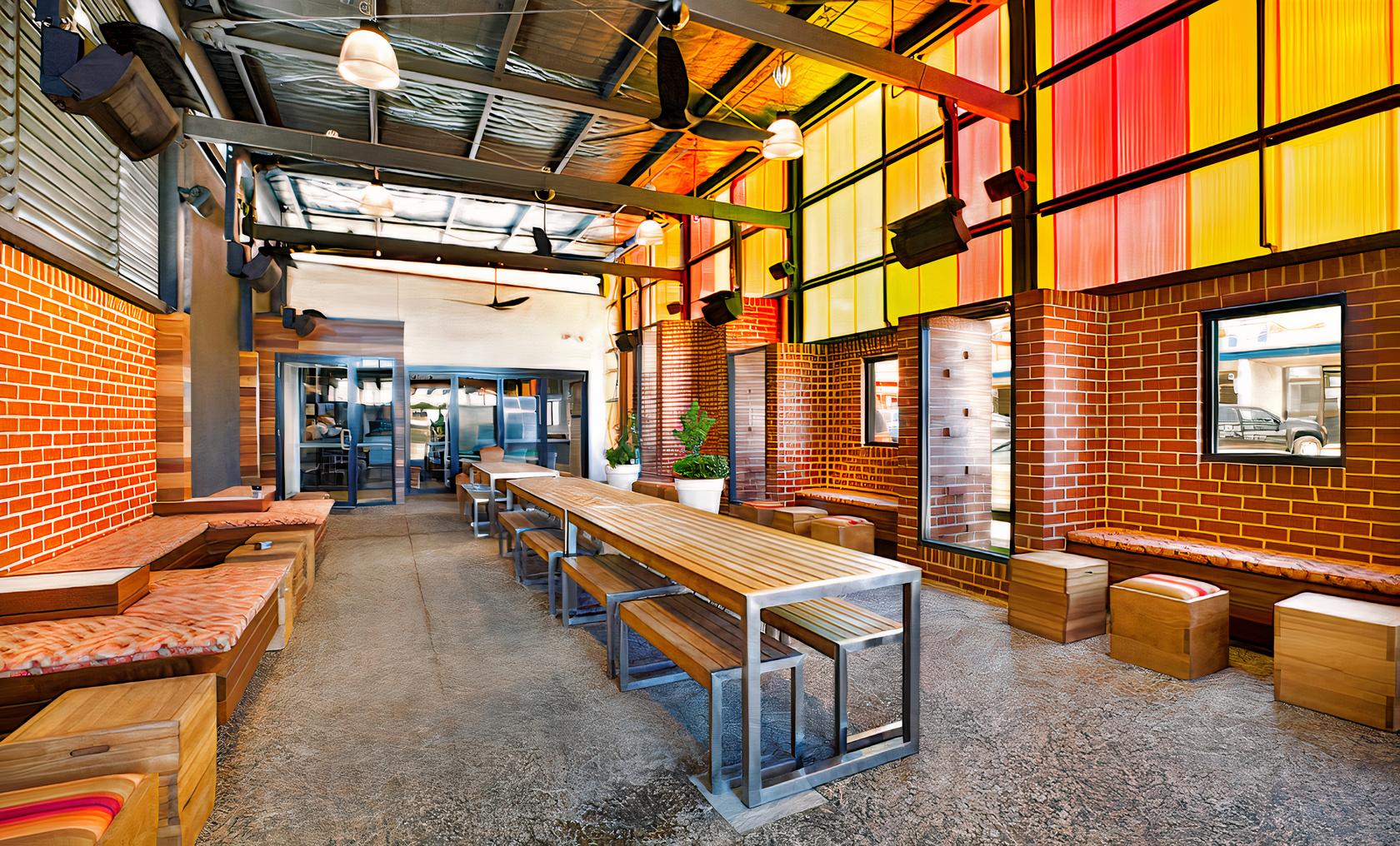 An event space in a pub with exposed brick walls, colorful translucent panels, and long wooden tables at Somerville Hotel.
