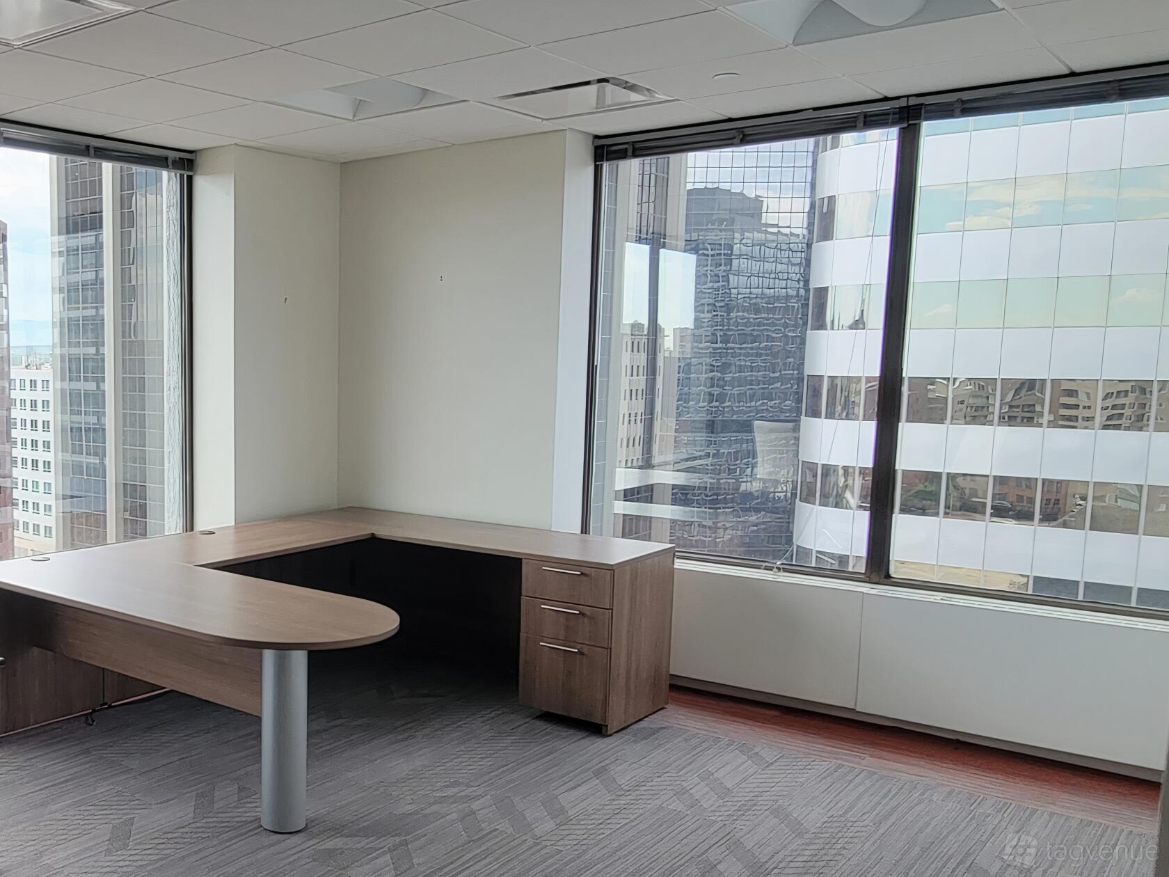 An office space with an L-shaped desk, floor-to-ceiling windows, and city views at Coalition Space Denver.
