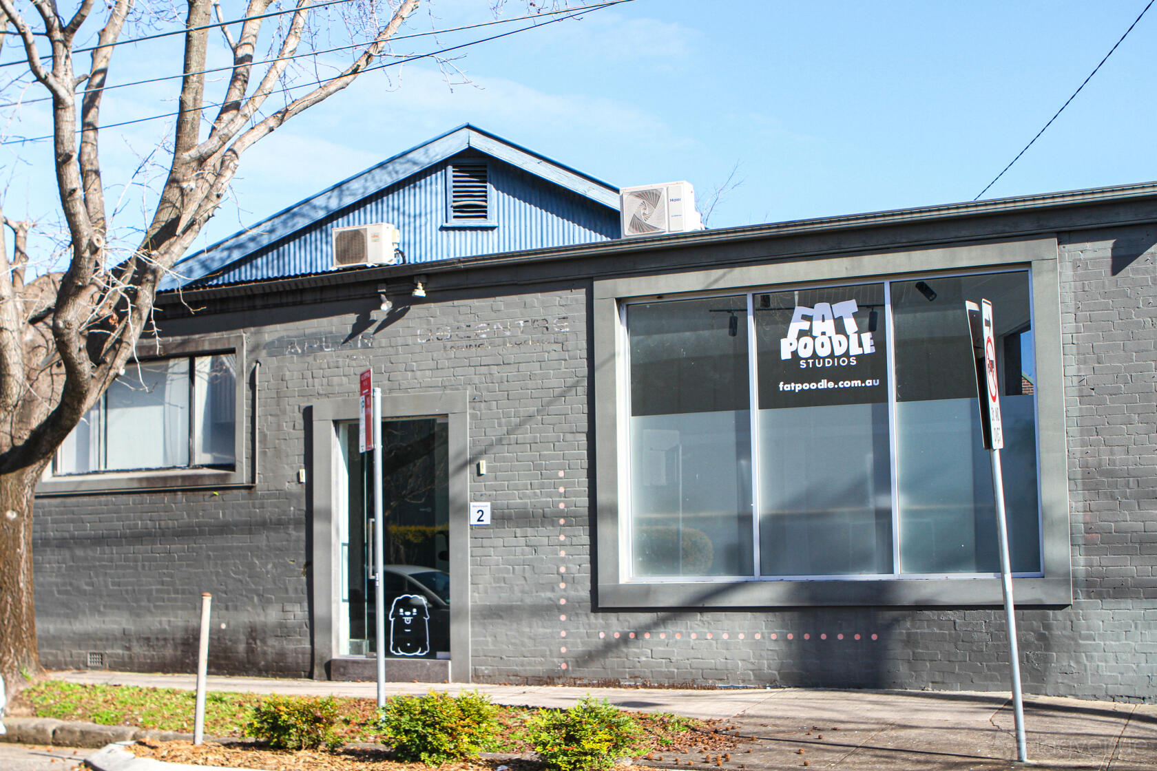 A gray brick apartment building with large front windows and Fat Poodle Studios signage at Fat Poodle Studios.